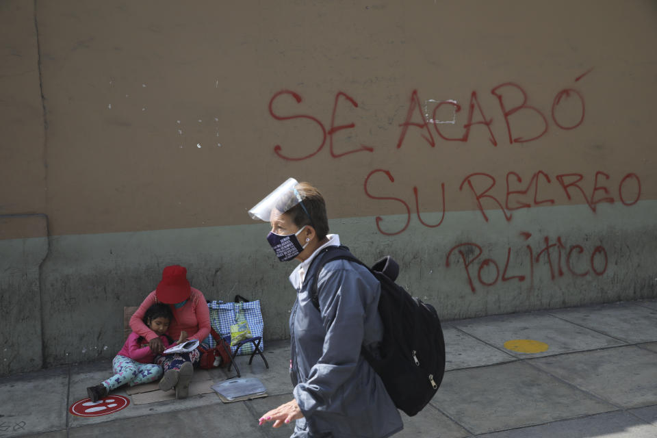 Graffiti written on a wall reads in Spanish "Your political recess is over," as Marta Perez teaches her 4-year-old daughter Diana Valentina to read as she sells candy near Congress where Francisco Sagasti will be sworn-in later in the day as the new, interim president at Congress in Lima, Peru, Tuesday, Nov. 17, 2020. Sagasti's appointment marks a tumultuous week in which thousands took to the streets outraged by Congress' decision to oust popular ex-President Martín Vizcarra. (AP Photo/Rodrigo Abd)