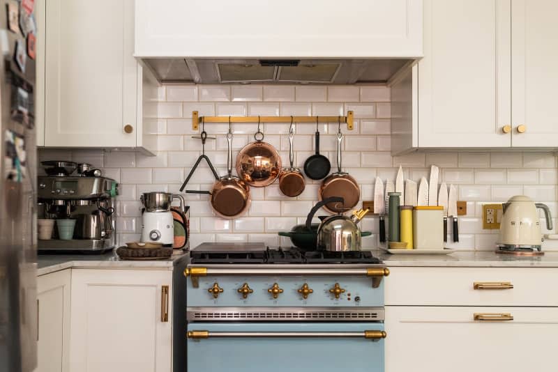 White kitchen with tile backsplash, blue oven white cabinets with gold pulls