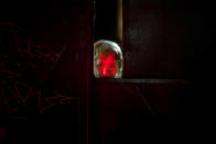 FILE - In this Monday, Nov. 2, 2015 photograph, a woman's face is lit by candles placed outside the Colectiv nightclub as she peers from behind the metal gate leading to the club in Bucharest, Romania. The Oscar-nominated Romanian documentary film “Collective” follows a group of journalists delving into the state of health care in the eastern European country in the wake of a deadly 2015 nightclub fire that left dozens of burned victims in need of complex treatment. What they revealed was decades of deep-rooted corruption, a heavily politicized system scarily lacking in care. (AP Photo/Vadim Ghirda, File)