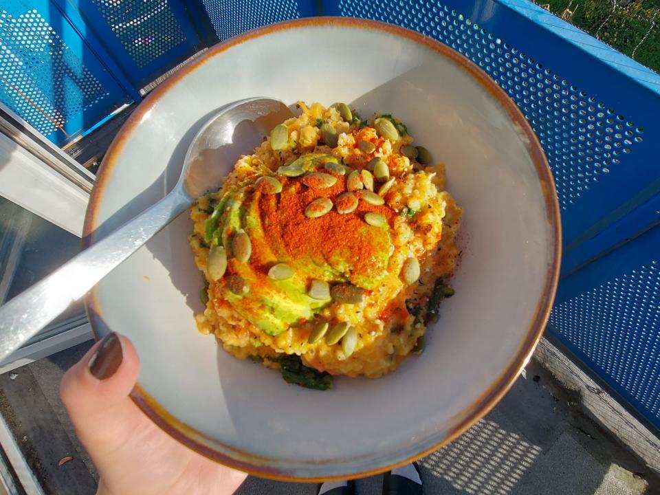 A white bowl with a spoon and savory oatmeal with avocado, pumpkin seeds, and paprika on top.