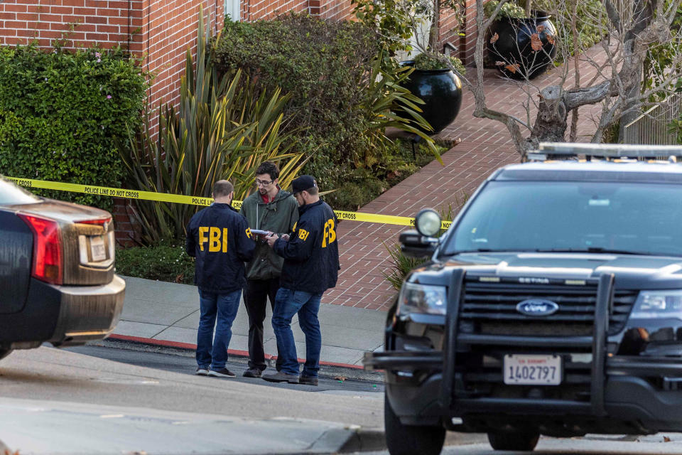 Three FBI agents confer by the yellow crime tape on the street outside the Pelosi home.