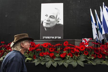 A man walks past the coffin of Israeli singer Arik Einstein, depicted in the placard, during a memorial ceremony before his funeral at Rabin square in Tel Aviv November 27, 2013. REUTERS/Nir Elias