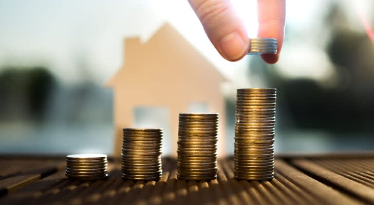 Coins stacked in front of graphic 2D cutout of house with sunlight shining on coins; growth in the housing market; housing stocks