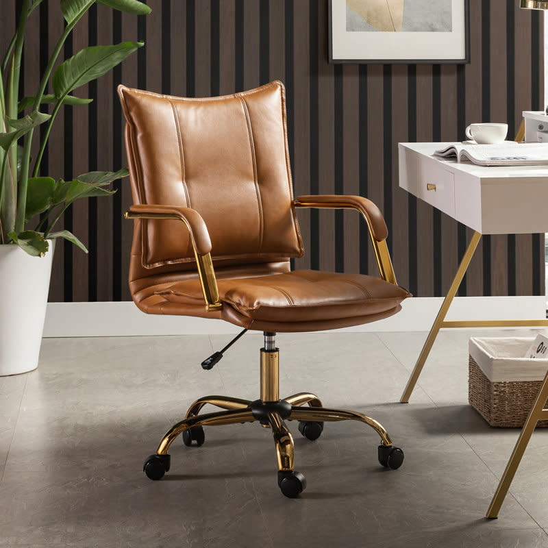 A stylish, modern brown leather office chair with gold accents is placed in a chic home office setting