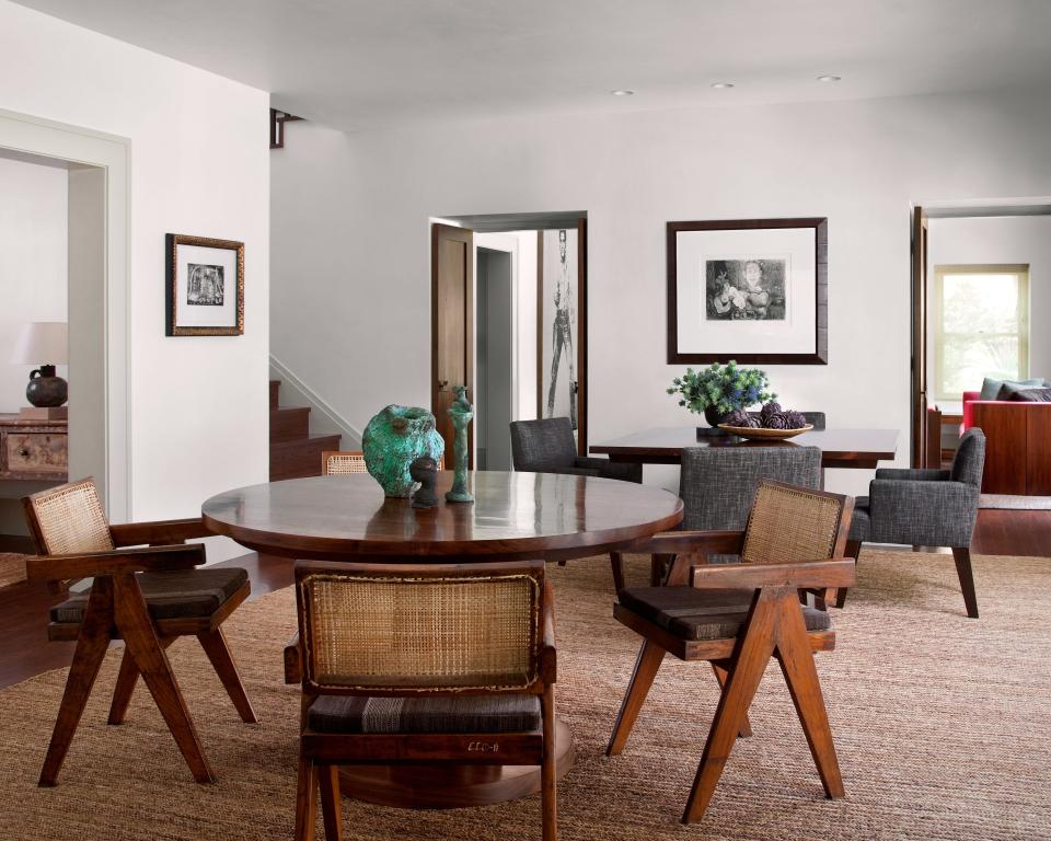 The dining room is outfitted with a pair of custom walnut tables, Pierre Jeanneret chairs with cushions made from vintage kilims, Picasso etchings, and small bronze sculptures by Harry Bertoia.