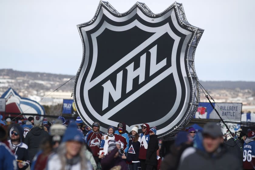 FILE - In this Feb. 15, 2020, file photo, fans pose below the NHL league logo at a display outside Falcon Stadium before an NHL Stadium Series outdoor hockey game between the Los Angeles Kings and Colorado Avalanche, at Air Force Academy, Colo. The uncertainty raised by coronavirus pandemic leads to experts providing a bleak short-term assessment on the NHL's financial bottom line, with some projecting revenues being cut by almost half. What's unclear is how large the impact might be until it can be determined when fans can resume attending games and if the league is able to complete this season. (AP Photo/David Zalubowski, File)