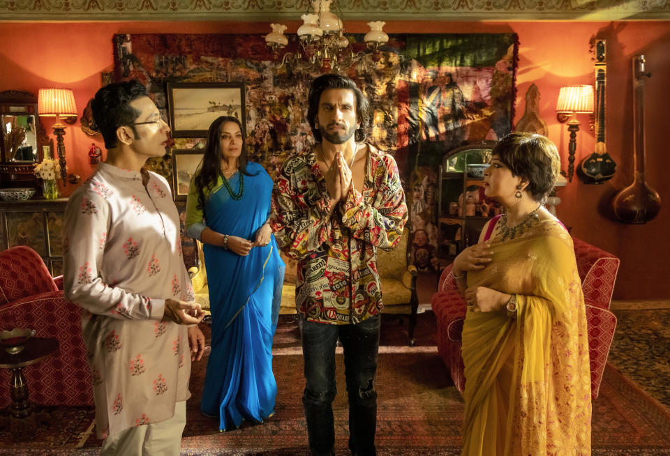 An Indian family stands in their living room, where the youngest male (20s, 30s) puts his palms together to pay respects to someone or something O.S.; still from "Rocky Aur Rani Kii Prem Kahaani."