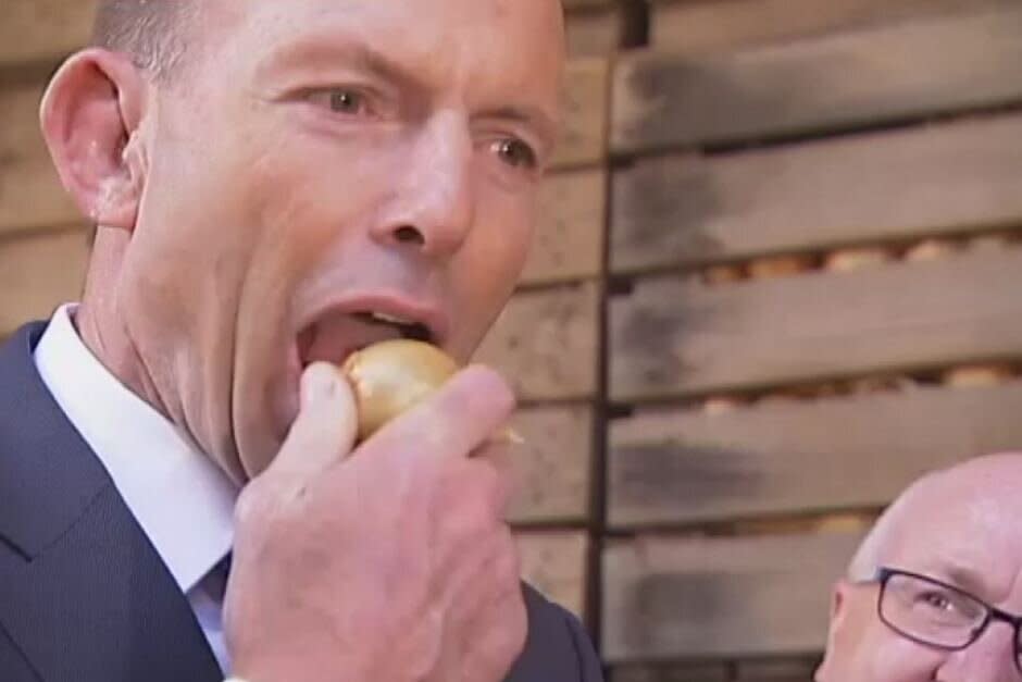 Tony Abbott eats a raw onion on a tour of Tasmanian onion farm in 2017. (Image: ABC News)