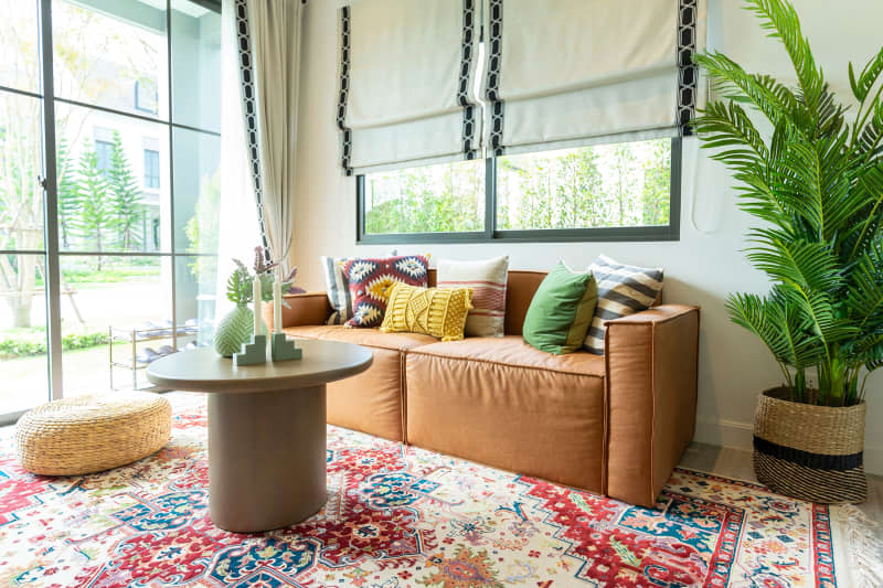 Living room in traditional British cottage furnished with modern looking furniture.  Green and yellow pillows on Leather sofa with green plant pot.