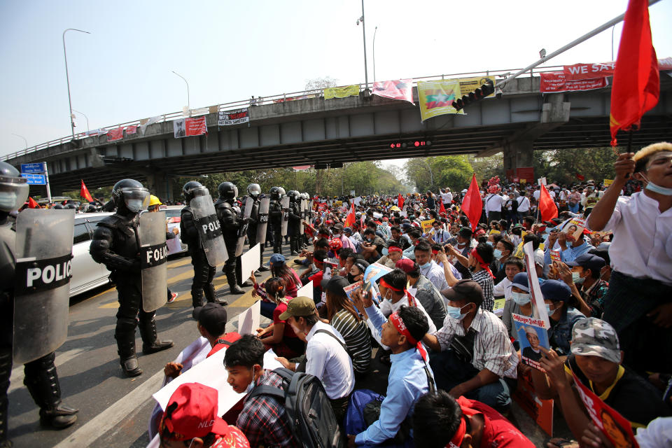 A row of riot police stand in front of anti-coup protesters seated on the road outside the Hledan Centre in Yangon, Myanmar Friday, Feb. 19, 2021. The daily protests campaigning for civil disobedience in Myanmar are increasingly focusing on businesses and government institutions that sustain the economy. (AP Photo)