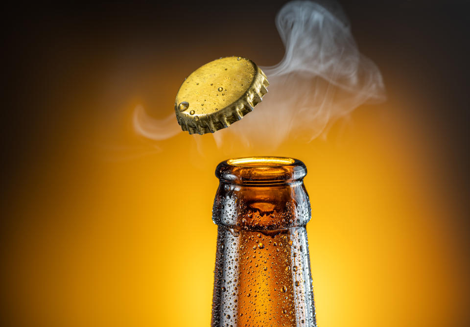 Opening of cold beer bottle - gas output and bottle cap in the air. Isolated on a yellow background.