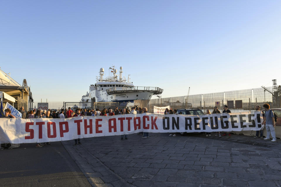 Protesters hold a banner reading "stop the attack on refugees" in front of the Norway-flagged Geo Barents ship operated by Doctors Without Borders, at harbor in Catania's port, Sicily, southern Italy, Monday, Oct. 7, 2022. The Geo Barents has been allowed Sunday to disembark 357 migrant that Italian authorities defined as "vulnerable people" and minors, while leaving another 215 people that were declared non-vulnerable blocked on board. (AP Photo/Salvatore Cavalli)