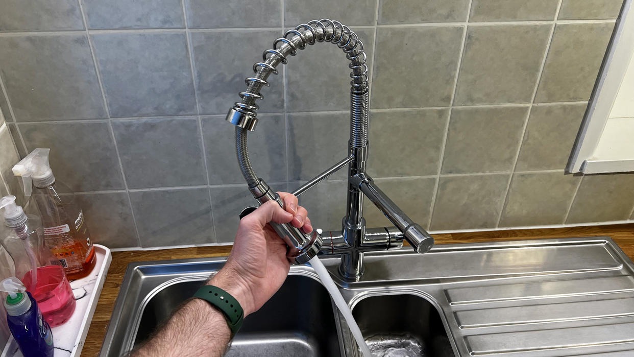  Fohen Flex tap in a kitchen, being held by a hand while water sprays. 