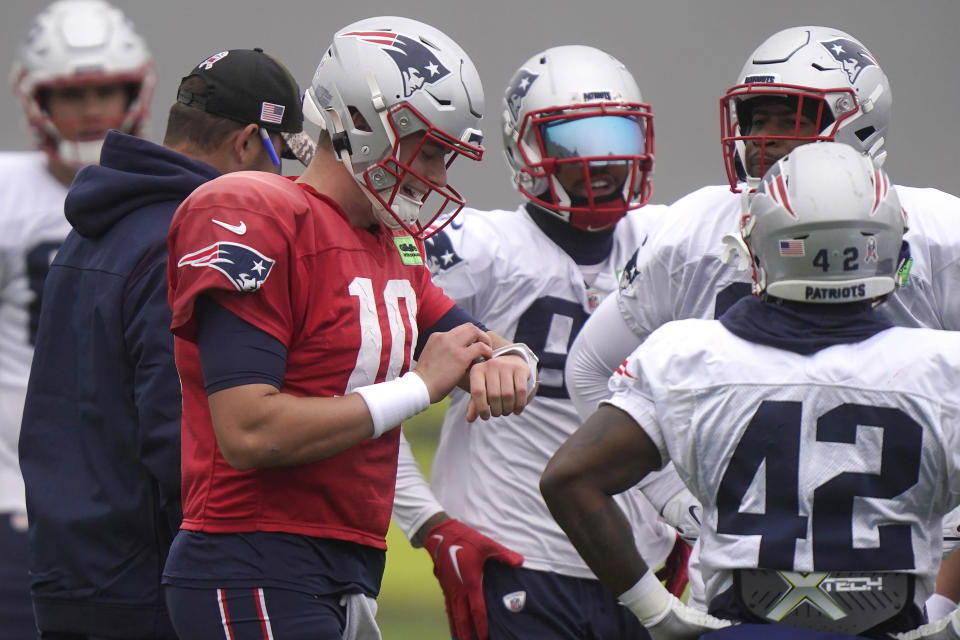 New England Patriots quarterback Mac Jones, center left, looks at his wrist band as running back J.J. Taylor (42) looks on during an NFL football practice, Wednesday, Nov. 16, 2022, in Foxborough, Mass. (AP Photo/Steven Senne)