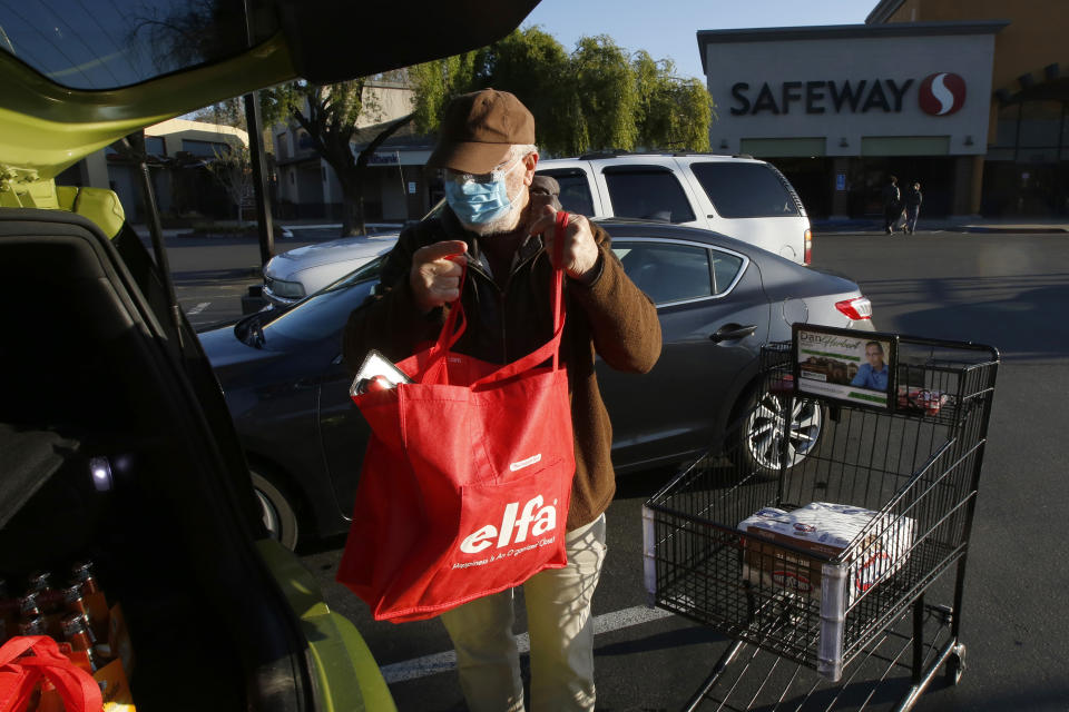 Wearing a mask for protection against the coronavirus, Henry Powell, puts his groceries in his car after shopping at a Safeway store in Sacramento, Calif., Thursday, March 19, 2020. Safeway is among the stores that are offering special shopping hours for seniors, like Powell, who is in his 70's, to get their groceries before opening to the rest of the public. (AP Photo/Rich Pedroncelli)