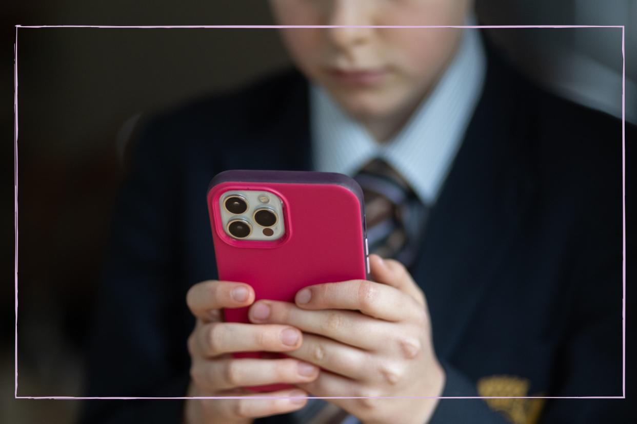  A close up of a boy in school uniform using an iPhone. 