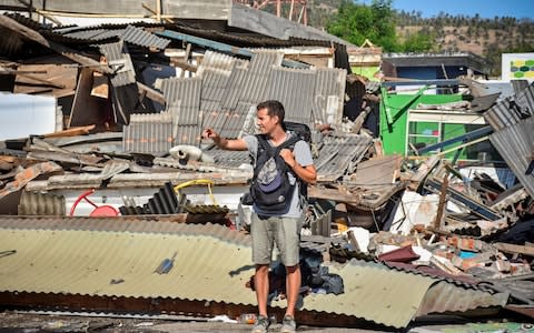 A foreign tourists stands near damaged buldings as he tries to flag down a car following a strong earthquake in Pemenang, North Lombok - Credit: Reuters