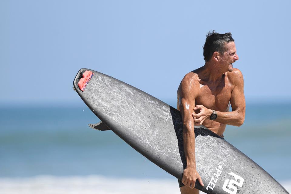 A surfer scratches his arm after reaching the beach at Fort Pierce Inlet State Park on Tuesday, Sept. 13, 2022. The moon jelly fish have been seen around the treasure coast, pulsing through the water and washing up on the shoreline. Surfers took advantage of the 5-8 foot swell on Tuesday, despite the influx of the stinging jellies. 