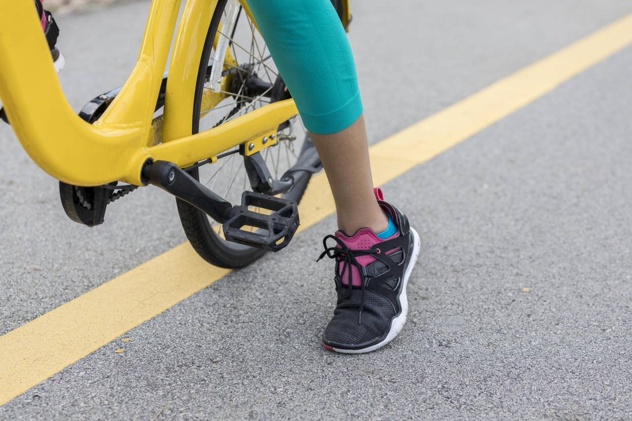 Unrecognizable female cyclist places her foot on the road after stopping.