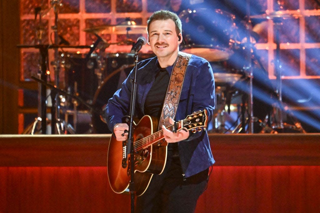 morgan wallen wearing a blue suit and holding guitar as he performs behind a microphone