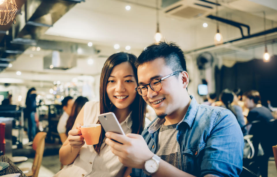 Cheerful young man and woman enjoying a coffee break while laughing and talking with smartphone in a cafe.