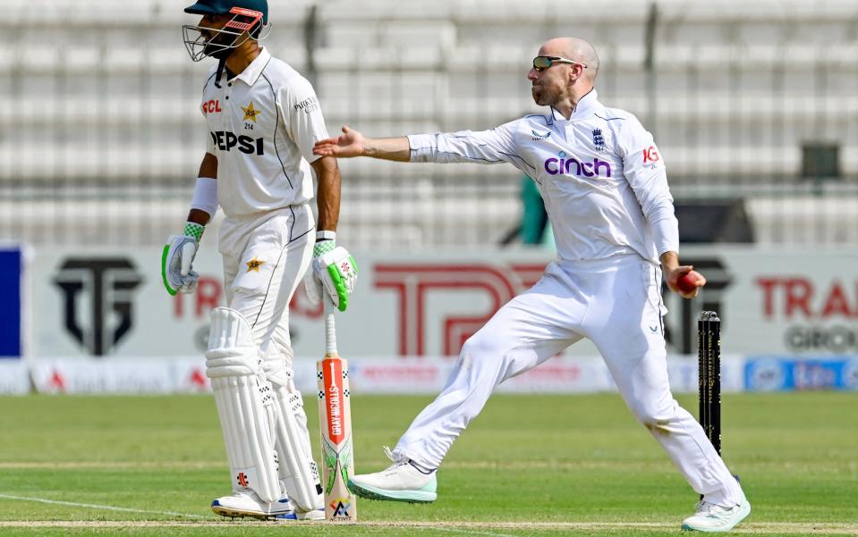 England's Jack Leach (R) delivers a ball as Pakistan's captain Shan Masood looks on during the first day of the first Test cricket match between Pakistan and England, at the Multan Cricket Stadium in Multan on October 7, 2024