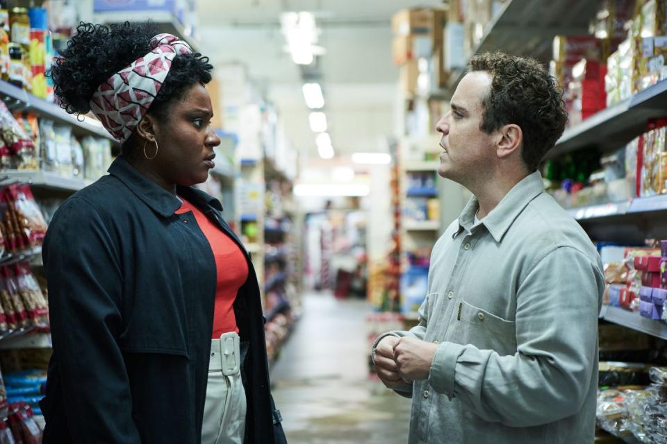 susan wokoma as fola and joshua mcguire as josh in cheaters season 1, a man and woman stand looking at each other in a supermarket