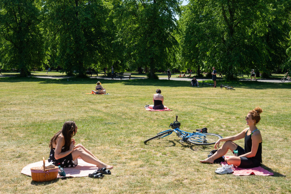 Two women observe social distancing whilst enjoying the hot weather in Greenwich Park, London.