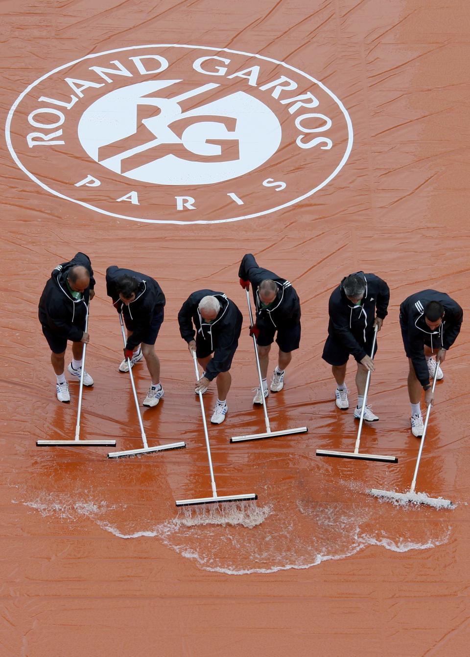 Workers sweep water off a tarp as rain interrupts a men's singles match between Novak Djokovic of Serbia and Joao Sousa of Portugal at the French Open tennis tournament at the Roland Garros stadium in Paris May 26, 2014. REUTERS/Gonzalo Fuentes (FRANCE - Tags: SPORT TENNIS)