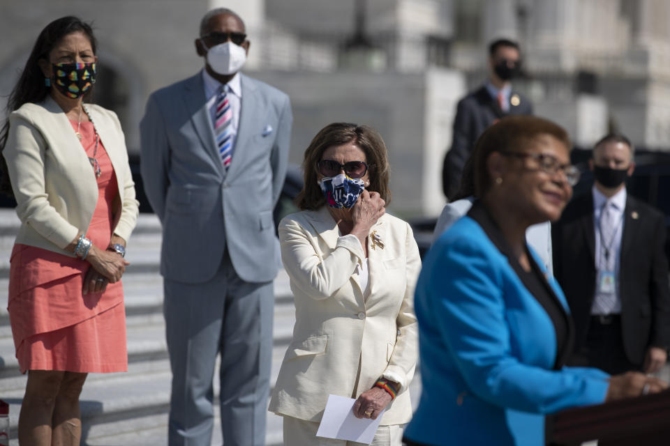 House Speaker Nancy Pelosi of Calif., adjusts her facemark as she stands with House Democrats spaced for social distancing, as Rep. Karen Bass, D-Calif., right, speaks during a news conference on the House East Front Steps on Capitol Hill in Washington, Thursday, June 25, 2020, ahead of the House vote on the George Floyd Justice in Policing Act of 2020. (AP Photo/Carolyn Kaster)