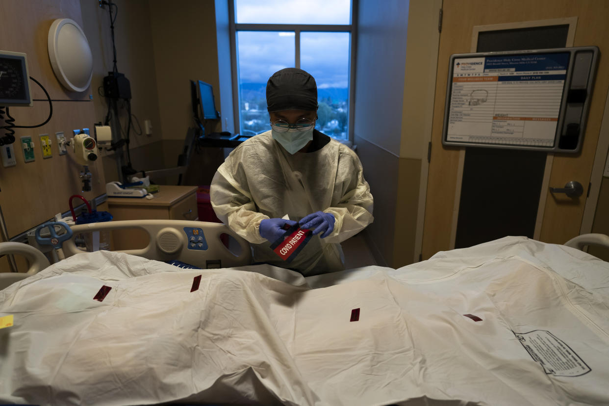 Registered nurse Bryan Hofilena attaches a "COVID Patient" sticker on a body bag of a patient who died of coronavirus at Providence Holy Cross Medical Center in Los Angeles, Tuesday, Dec. 14, 2021. Many hospitals across the country are struggling to cope with burnout among doctors, nurses and other workers. Already buffeted by a crush of patients from the ongoing surge of the coronavirus's delta variant, they're now bracing for the fallout of another highly transmissible mutation. (AP Photo/Jae C. Hong)