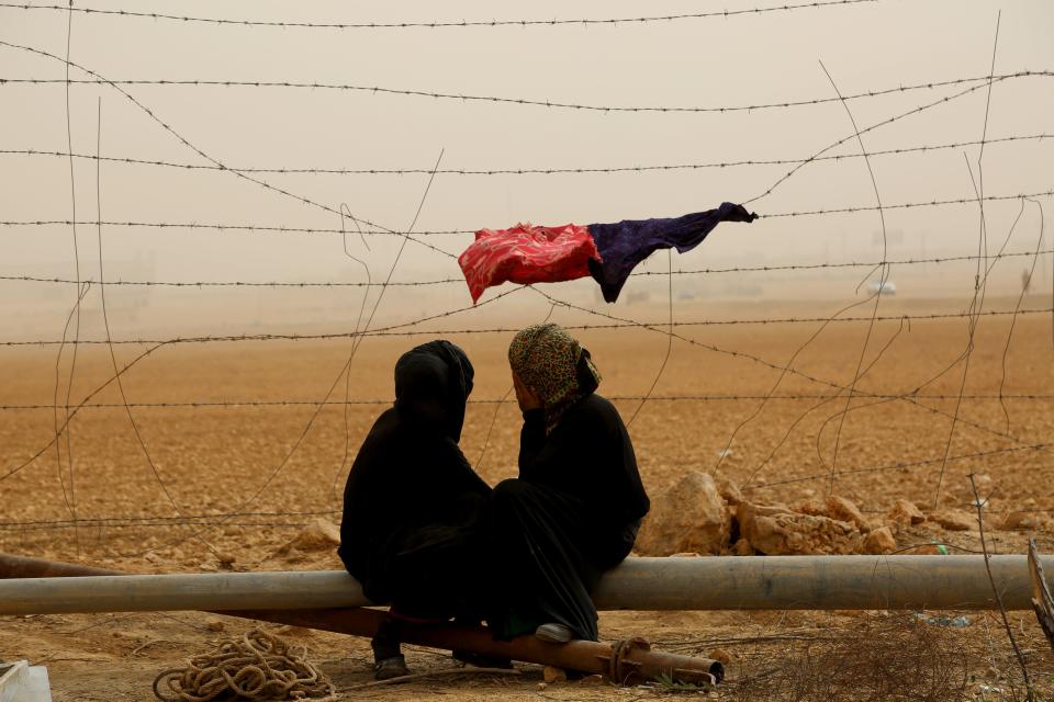 Syrian women sit next to the fence during a sandstorm at a temporary refugee camp in the village of Ain Issa, housing people who fled Islamic State group's Syrian stronghold Raqa, some 50 kilometers (30 miles) north of the group's de facto capital on November 10, 2016.