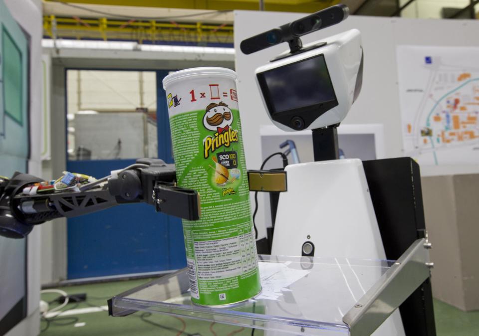 A robotic arm, left, puts a package of Pringles on the serving tray of another robot to deliver it to an imaginary patient in a mock hospital room at the Technical University of Eindhoven, Netherlands, Wednesday Jan. 15, 2014. A group of five of Europe's top technical universities, together with technology conglomerate Royal Philips NV, are launching an open-source system dubbed "RoboEarth" Thursday. The heart of the mission is to accelerate the development of robots and robotic services via efficient communication with a network, or "cloud". (AP Photo/Peter Dejong)