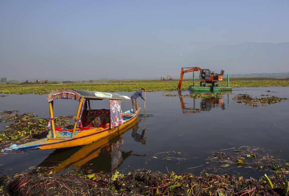 A Kashmiri boatman rows his boat as a de-weeding machine works at Dal lake in Srinagar, Indian controlled Kashmir, Tuesday, Sept. 14, 2021. Weeds, silt and untreated sewage are increasingly choking the sprawling scenic lake, which dominates the city and draws tens of thousands of tourists each year. (AP Photo/Mukhtar Khan)