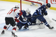 Winnipeg Jets goaltender Connor Hellebuyck (37) makes a save on New Jersey Devils' Pavel Zacha (37) as Jets' Neal Pionk (4) defends during the first period of an NHL hockey game Friday, Dec. 3, 2021, in Winnipeg, Manitoba. (John Woods/The Canadian Press via AP)