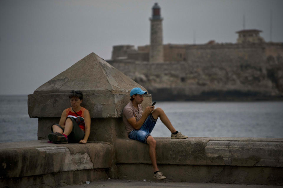 En esta fotografía del miércoles 20 de febrero de 2019, un hombre chatea usando su celular junto a una mujer que lee un libro en el malecón de La Habana, en Cuba. En los dos meses y medio desde que Cuba le permitió a los ciudadanos tener acceso a internet a través de los teléfonos celulares, hay cambios rápidos, sutiles pero palpables, a medida que los cubanos desafían en línea a las autoridades, publican fotografías de baños escolares sucios e introducen a la era digital a la que fue alguna vez una de las naciones menos conectadas a internet. (AP Foto/Ramón Espinosa)