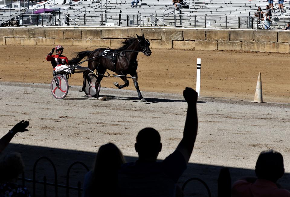 Scott Cisco waves to race fans as he drives Fear Our Fayth past the finish line in the 2-year-old Fillies first division race on Wednesday, Oct. 13, during the Fairfield County Fair's first day of harness racing.