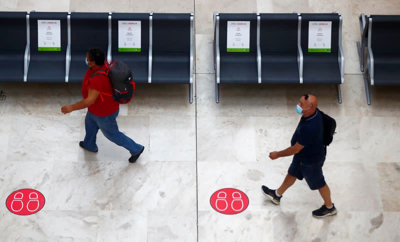 Pasajeros con mascarillas pasan junto a unos carteles que informan del distanciamiento social a su llegada desde París al aeropuerto Adolfo Suárez Madrid-Barajas, en Madrid, España