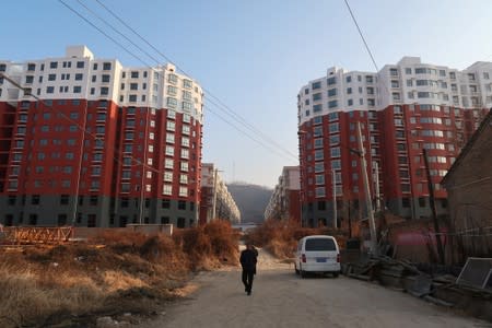 Man walks near a shantytown to be redeveloped, in front of apartment buildings, in Fu county in the south of Yanan