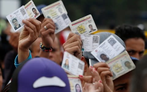 Venezuelan citizens hold up their identification cards for inspection by the Colombian immigration police in Cucuta - Credit: AP Photo/Fernando Vergara