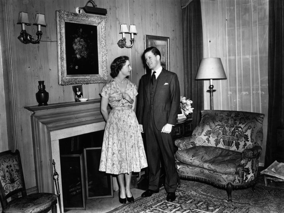 A black and white photo of Princess Diana's parents in front of a fireplace and large leather chair.