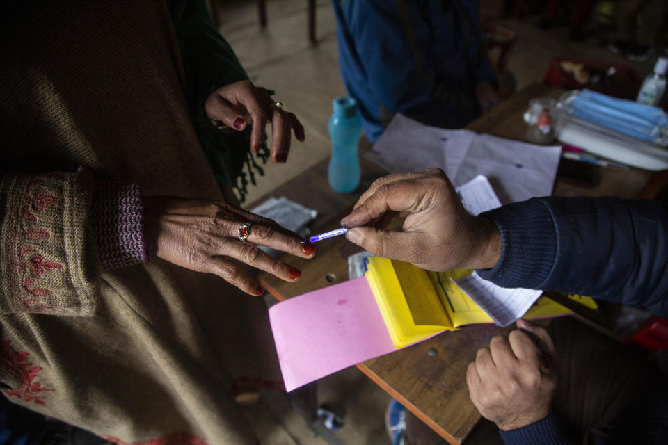 A local poling officer applies indelible ink mark on the finger of a Kashmiri casting her votes during the first phase of District Development Councils election on the outskirts of Srinagar, Indian controlled Kashmir, Saturday, Nov. 28, 2020. Thousands of people in Indian-controlled Kashmir voted Saturday amid tight security and freezing cold temperatures in the first phase of local elections, the first since New Delhi revoked the disputed region's semiautonomous status. (AP Photo/Mukhtar Khan)