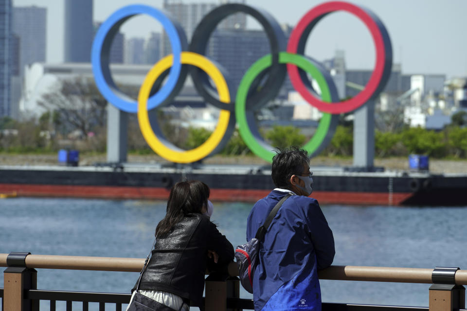 A man and a woman stand with a backdrop of the Olympic rings floating in the water in the Odaiba section Thursday, March 18, 2021, in Tokyo. Tokyo Olympics creative director Hiroshi Sasaki is resigning after making demeaning comments about Naomi Watanabe, a well-known female celebrity. Sasaki who was in charge of the opening and closing ceremonies for the Olympics, told planning staff members last year that Watanabe could perform in the ceremony as an “Olympig.” (AP Photo/Eugene Hoshiko)