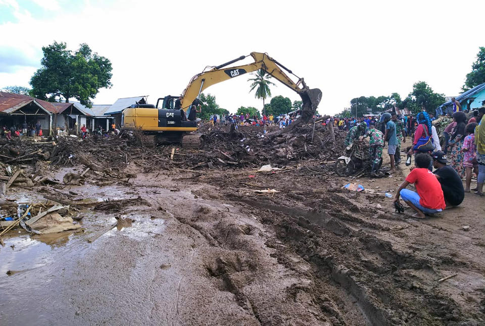 People watch as an excavator clears debris at a flood-affected area in Waiwerang, on Adonara Island, East Nusa Tenggara province, Indonesia, Tuesday, April 6, 2021. Rescuers in remote eastern Indonesia were digging through the debris of a landslide Tuesday in search of people believed to be buried in one of several disasters brought on by severe weather in the Southeast Asian nation and neighboring East Timor. (AP Photo/Rofinus Monteiro)