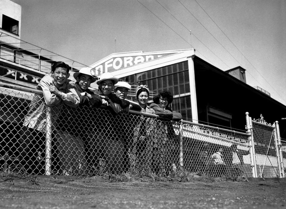 Six people of Japanese ancestry lean over a fence railing.