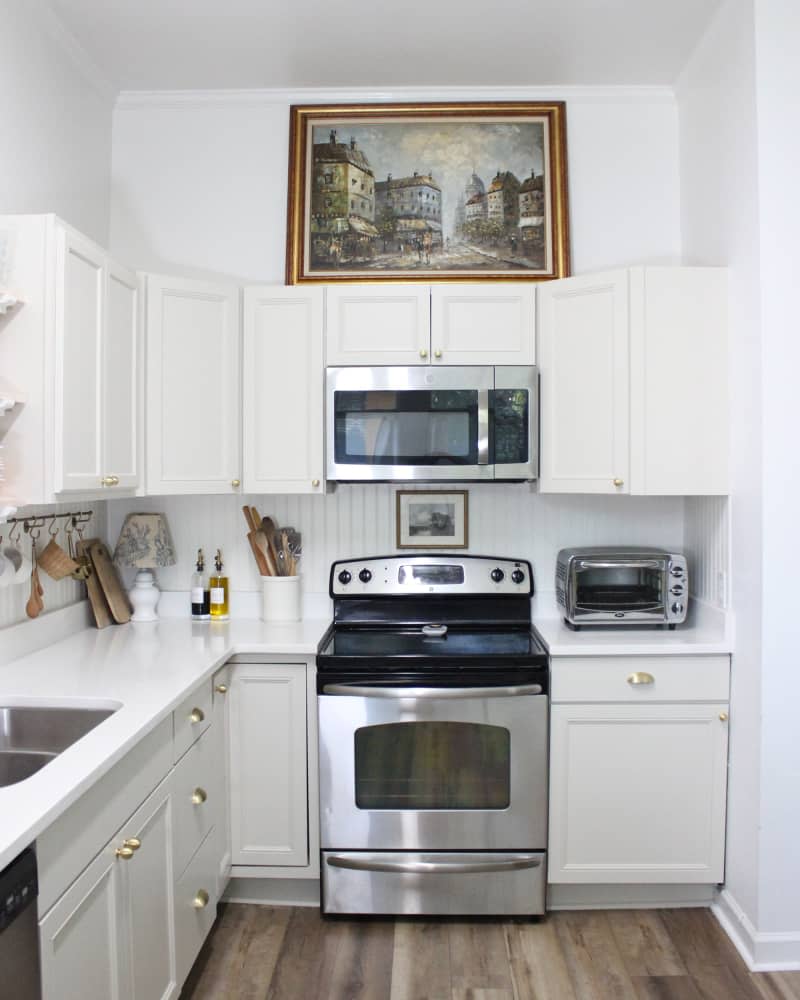 The renovated white kitchen features white cabinetry with gold hardware.