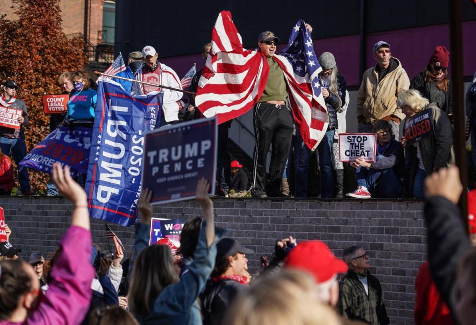 Michael Foy of Wixom, Michigan, holds his flag open while standing above the crowd gathered for a rally in support of President Trump outside of the TCF Center in Detroit on Friday, Nov 6, 2020 where the absentee ballot count for the city of Detroit took place.