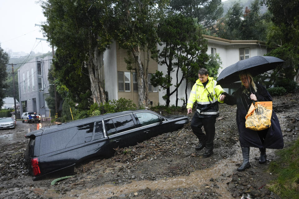 A first responder helps a resident evacuate from a neighborhood after a mudslide, Monday, Feb. 5, 2024, in the Beverly Crest area of Los Angeles. A storm of historic proportions unleashed record levels of rain over parts of Los Angeles on Monday, endangering the city's large homeless population, sending mud and boulders down hillsides dotted with multimillion-dollar homes and knocking out power for more than a million people in California. (AP Photo/Marcio Jose Sanchez)