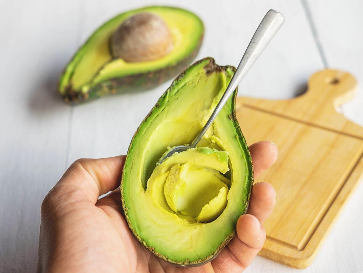 Half an avocado with a spoon in it, mid-scoop.