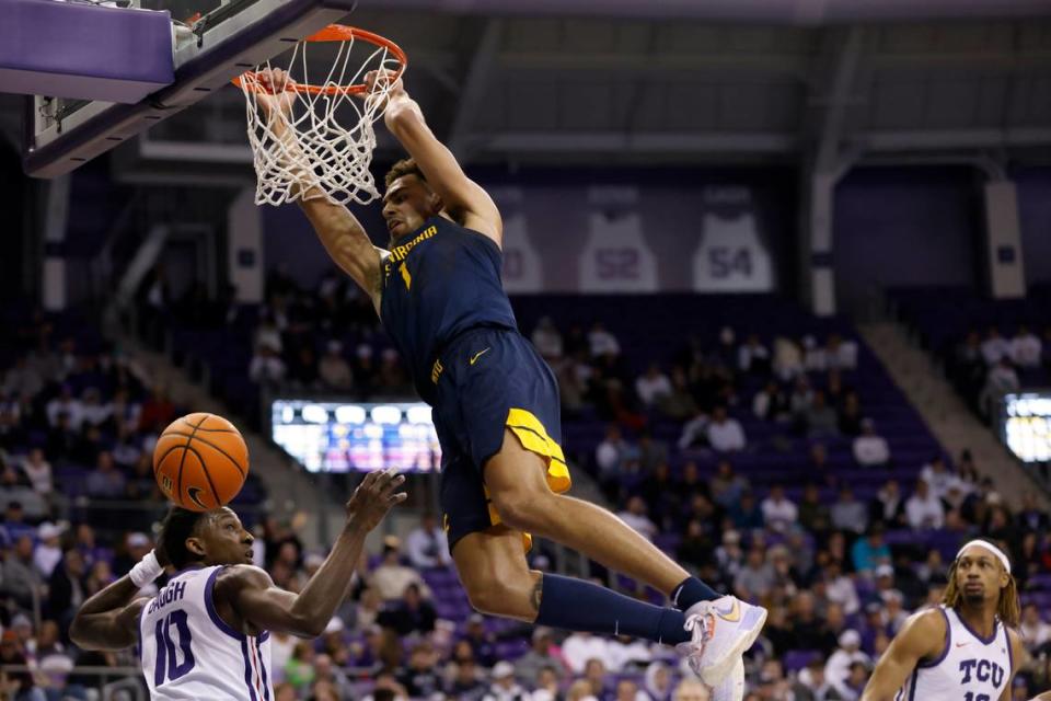 West Virginia forward Emmitt Matthews Jr. (1) hangs on the rim after dunking as TCU’s Damion Baugh (10) and Xavier Cork, right, look on in the second half of an NCAA college basketball game, Tuesday, Jan. 31, 2023, in Fort Worth, Texas. (AP Photo/Ron Jenkins)